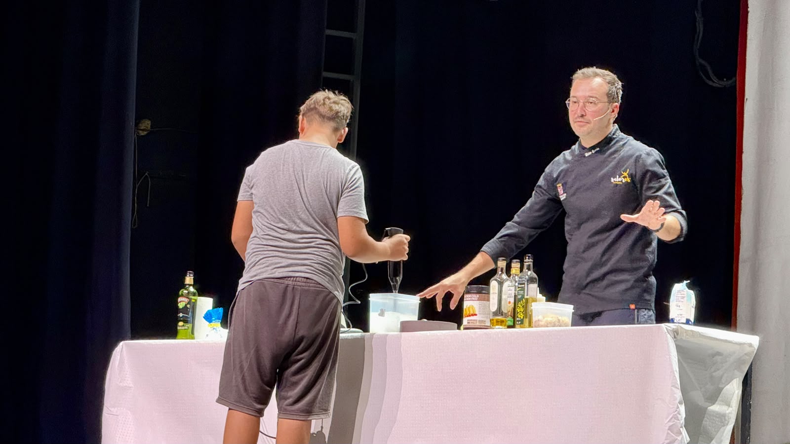 El chef David Hernández Papis Martínez explica la receta mientras un alumno usa la batidora en el escenario · Innova Humana